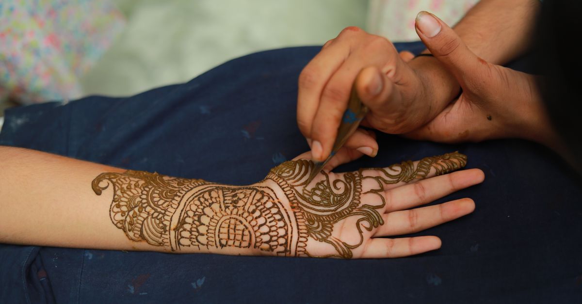 Intricate henna being applied to a bride's hands at a mehndi ceremony